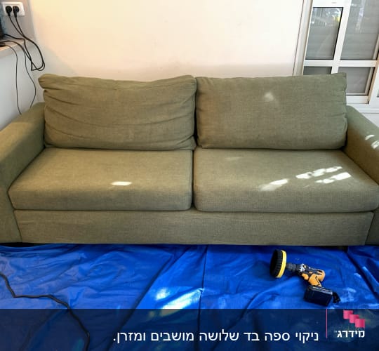 ספה ירוקה עם מכונת ניקוי על יריעת פלסטיק כחולה